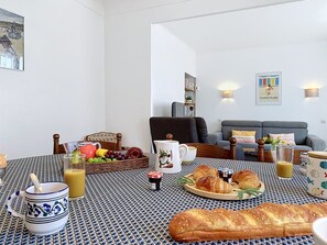 A living room with a dining area, featuring a table set with food and drinks, a sofa, and a bookshelf. - Claire Joie by Interhome (Saint Brevin les Pins)