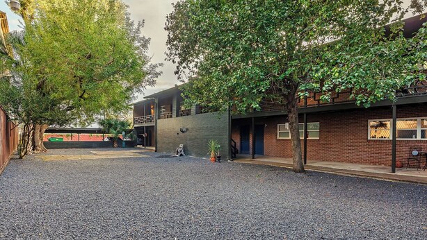 A courtyard with a gravel ground, two-story buildings with brick and metal facades, and trees providing shade. - The Montrose Hideaway, Downtown, Medical Center 07 (Houston)