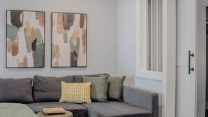 A modern living room with a grey sofa, a small ottoman, and abstract artwork on the wall. - The Montrose Hideaway, Downtown, Medical Center 07 (Houston)