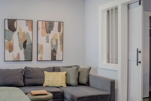 Ein modernes Wohnzimmer mit einem grauen Sofa, einem kleinen Hocker und abstrakter Kunst an der Wand.