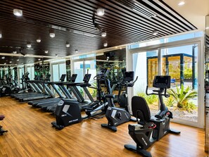 Et fitnessrum med flere konditionsmaskiner, trægulv og store vinduer med udsigt til det fri.