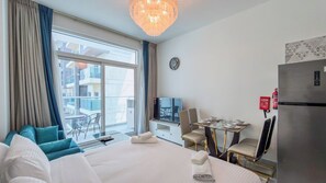 Ein Hotelzimmer mit Bett, Fernseher, Esstisch mit Stühlen, Kühlschrank und Blick auf den Balkon.