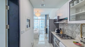A modern kitchen with a gas stove, microwave, and a view to the outside. - Pearlz By Danube Residences - Al Furjan (Dubai)