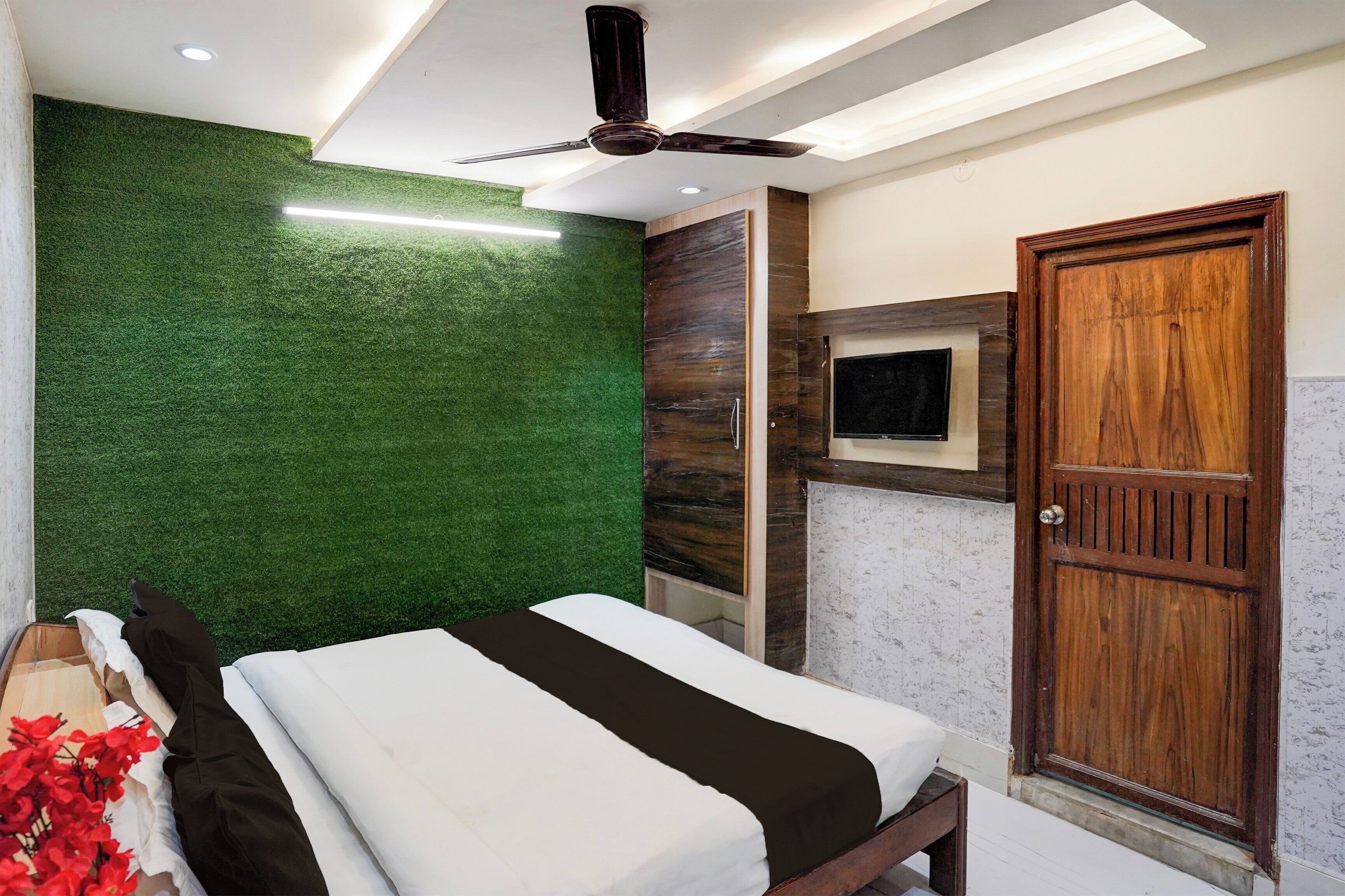Un dormitorio con cama, ventilador de techo, televisión montada en la pared y puerta de madera.