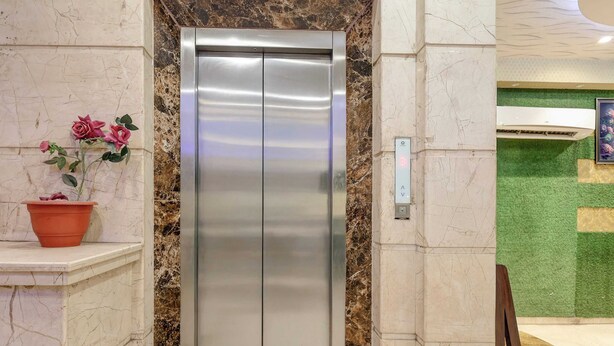 A modern elevator with a metallic finish, marble wall surrounds, and a potted plant on the left. - Collection O Kanpur Central Railway (Kanpur)