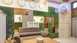 A lobby with a sofa, a coffee table, and a clock displaying times for New Delhi, Tokyo, and New York. - Collection O Kanpur Central Railway (Kanpur)