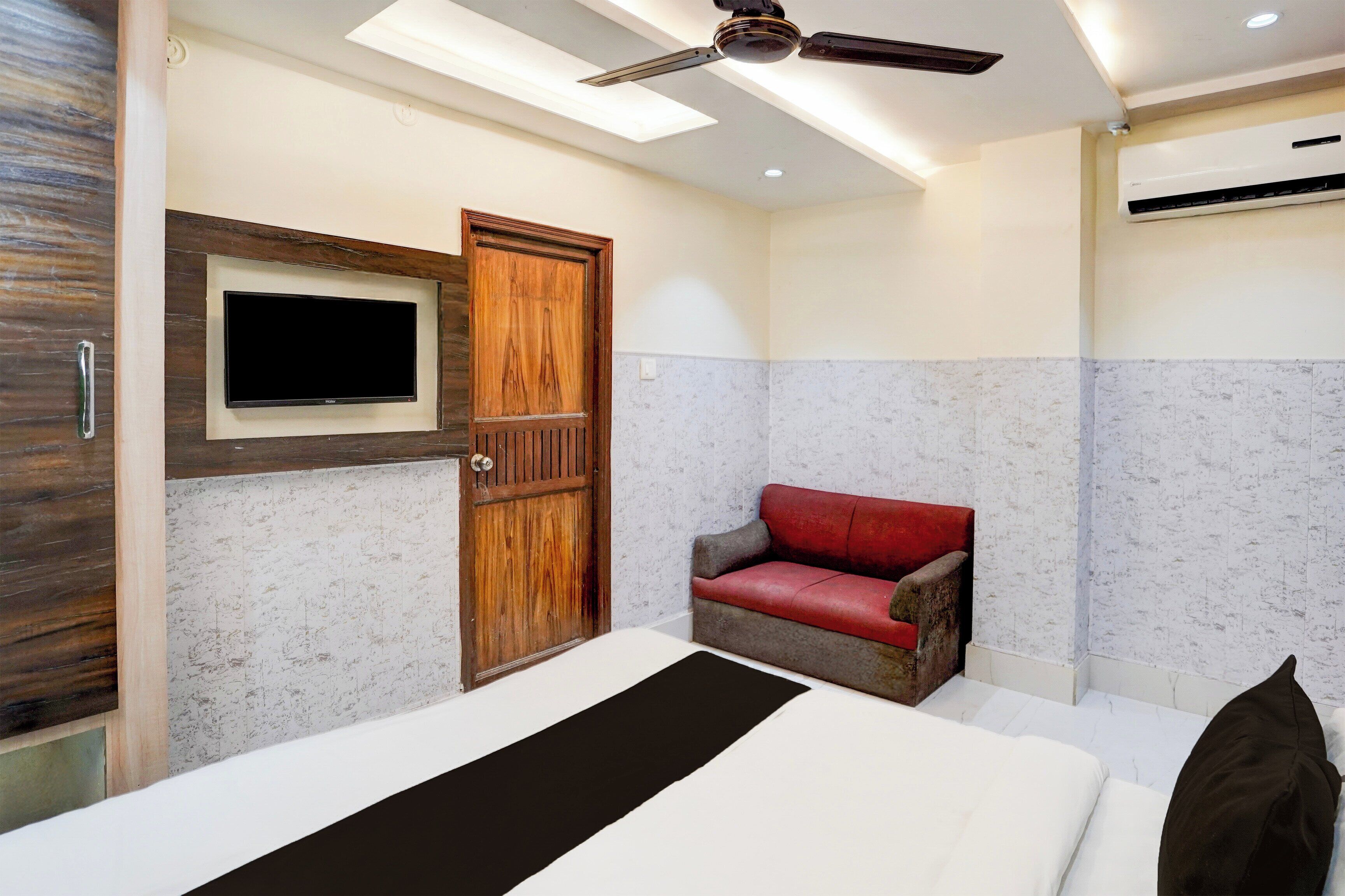 A bedroom with a bed, a television mounted on the wall, a ceiling fan, and a red leather chair.