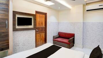 A bedroom with a bed, a television mounted on the wall, a ceiling fan, and a red leather chair.
