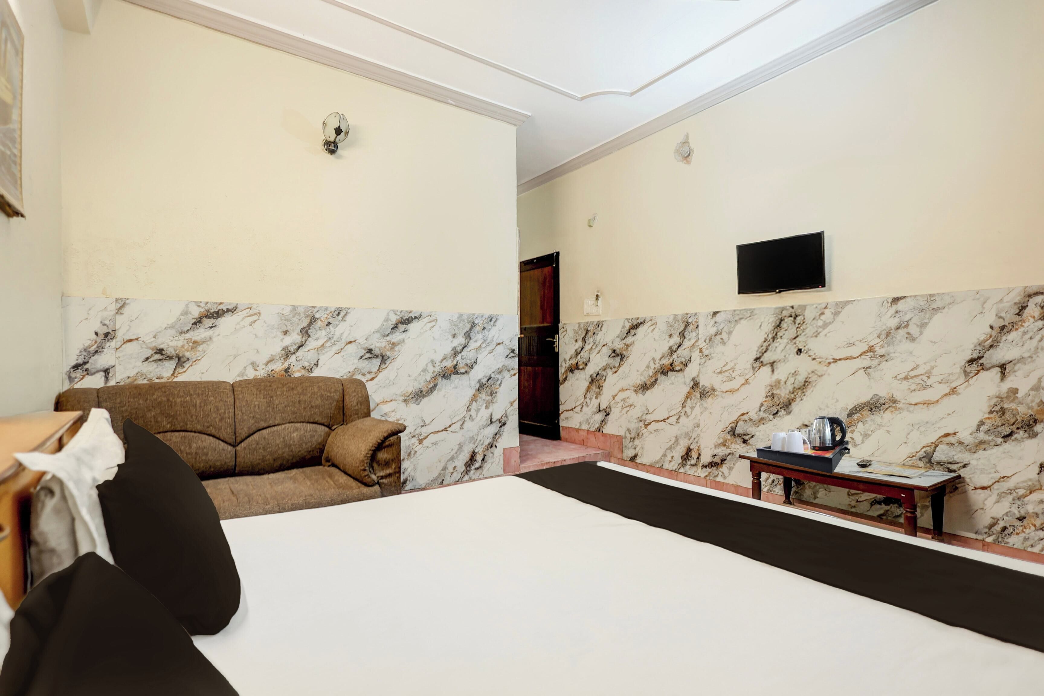 A hotel room with a bed, a sofa, a television, and a small table with a tray of items.