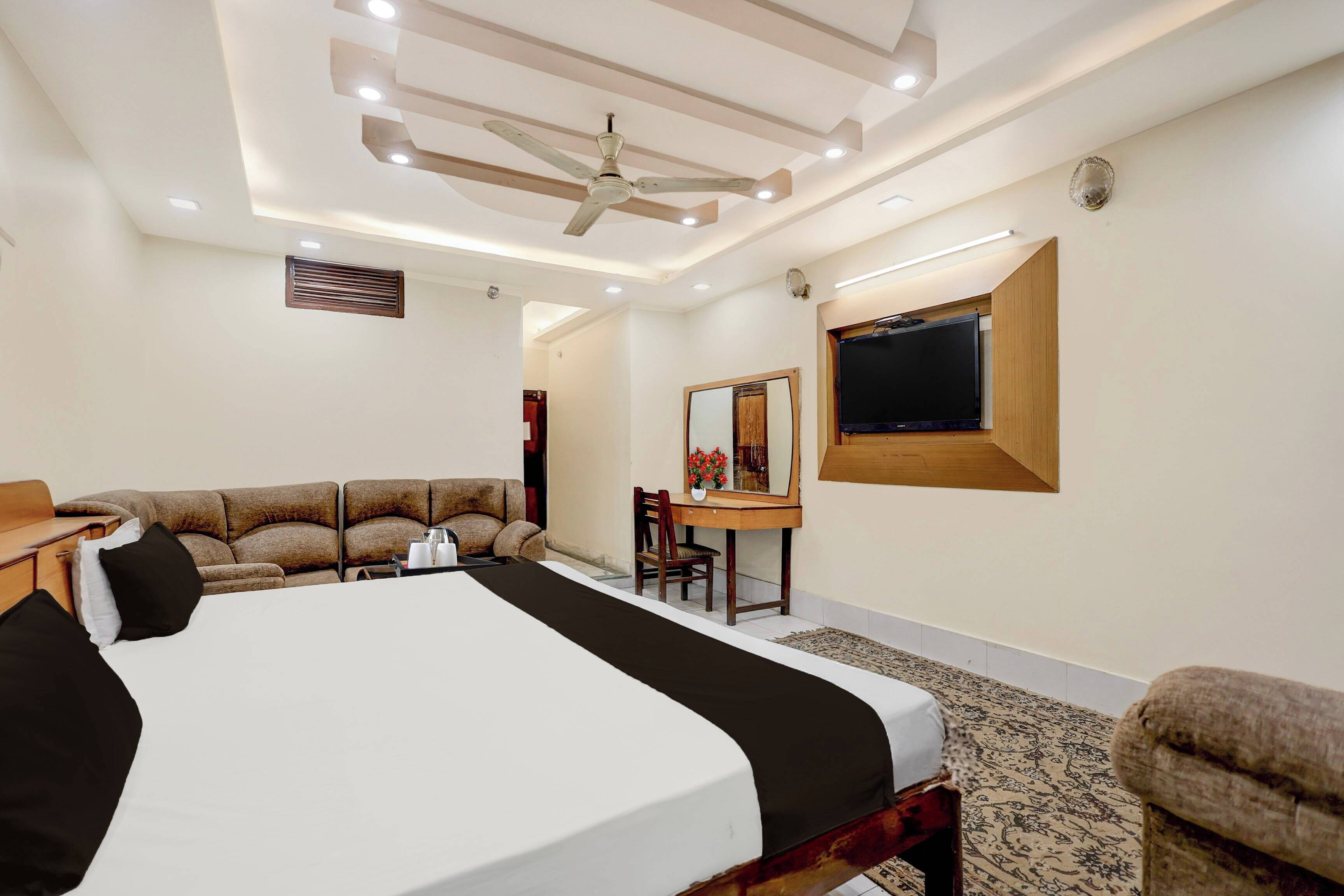 Habitación de hotel con una cama grande, un escritorio, una silla, un ventilador de techo y un televisor de pantalla plana montado en la pared.