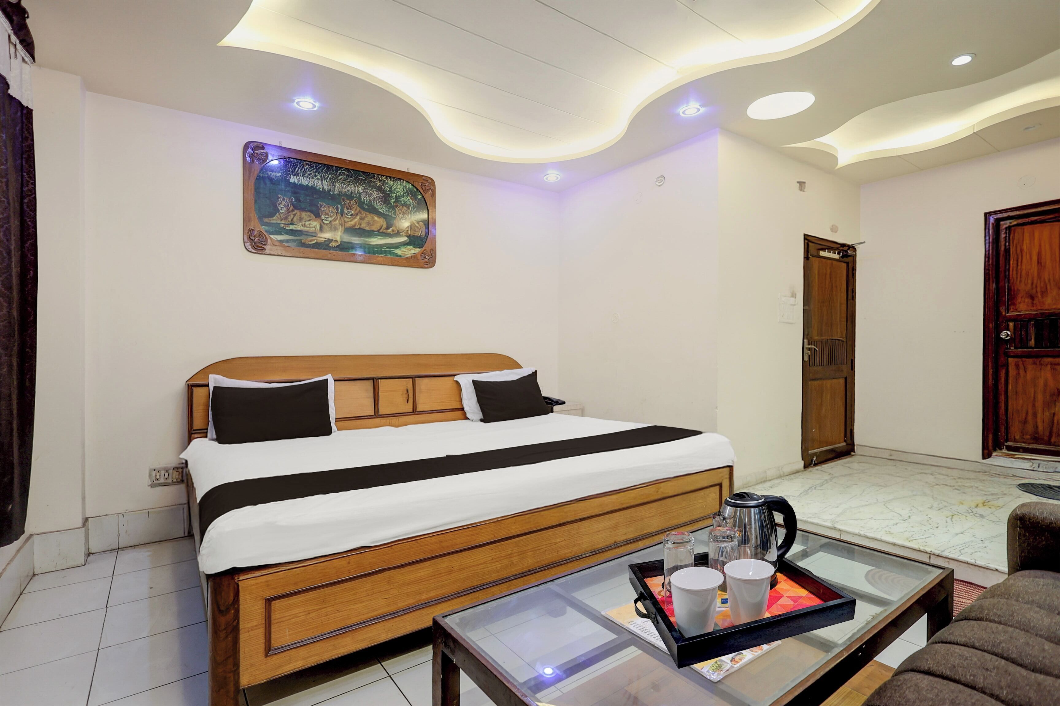 A hotel room with a wooden bed, a painting on the wall, a coffee table with a tray, and a door.