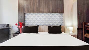 Hotelkamer met een groot bed, twee zwarte kussens, een nachtkastje met een lamp, een vaas met rode bloemen en een houten garderobe.