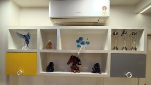 Una habitación con un equipo de aire acondicionado blanco, una estantería con adornos, un armario amarillo y un armario gris.