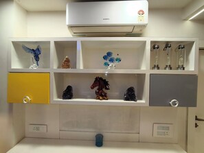 Ein Zimmer mit einer weißen Klimaanlage, einem Regal mit Dekoration, einem gelben Schrank und einem grauen Schrank.