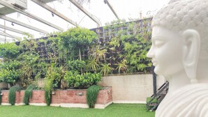 Una estatua blanca en un jardín con un muro de ladrillo y diversas plantas.