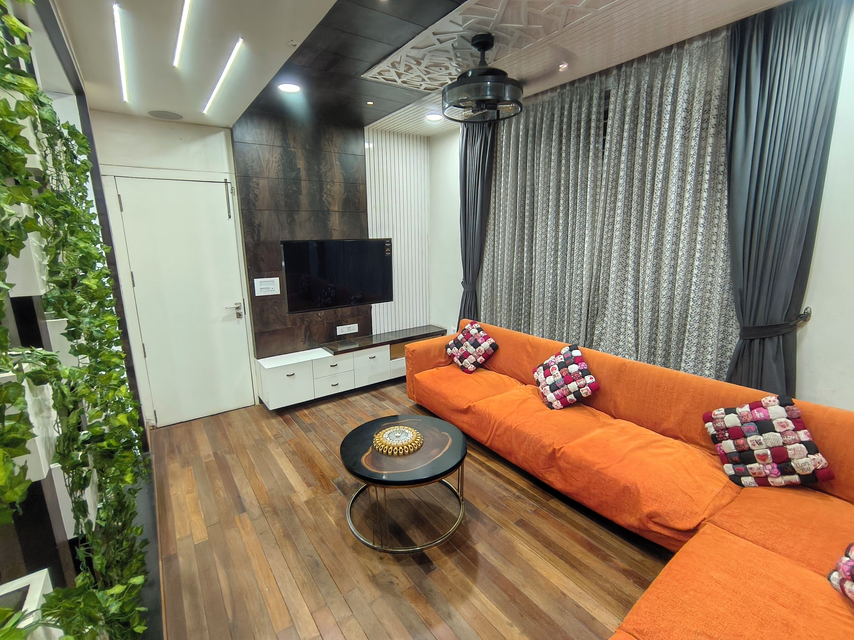 A modern living room with a sectional sofa, a flat-screen TV, a coffee table, and a ceiling fan.