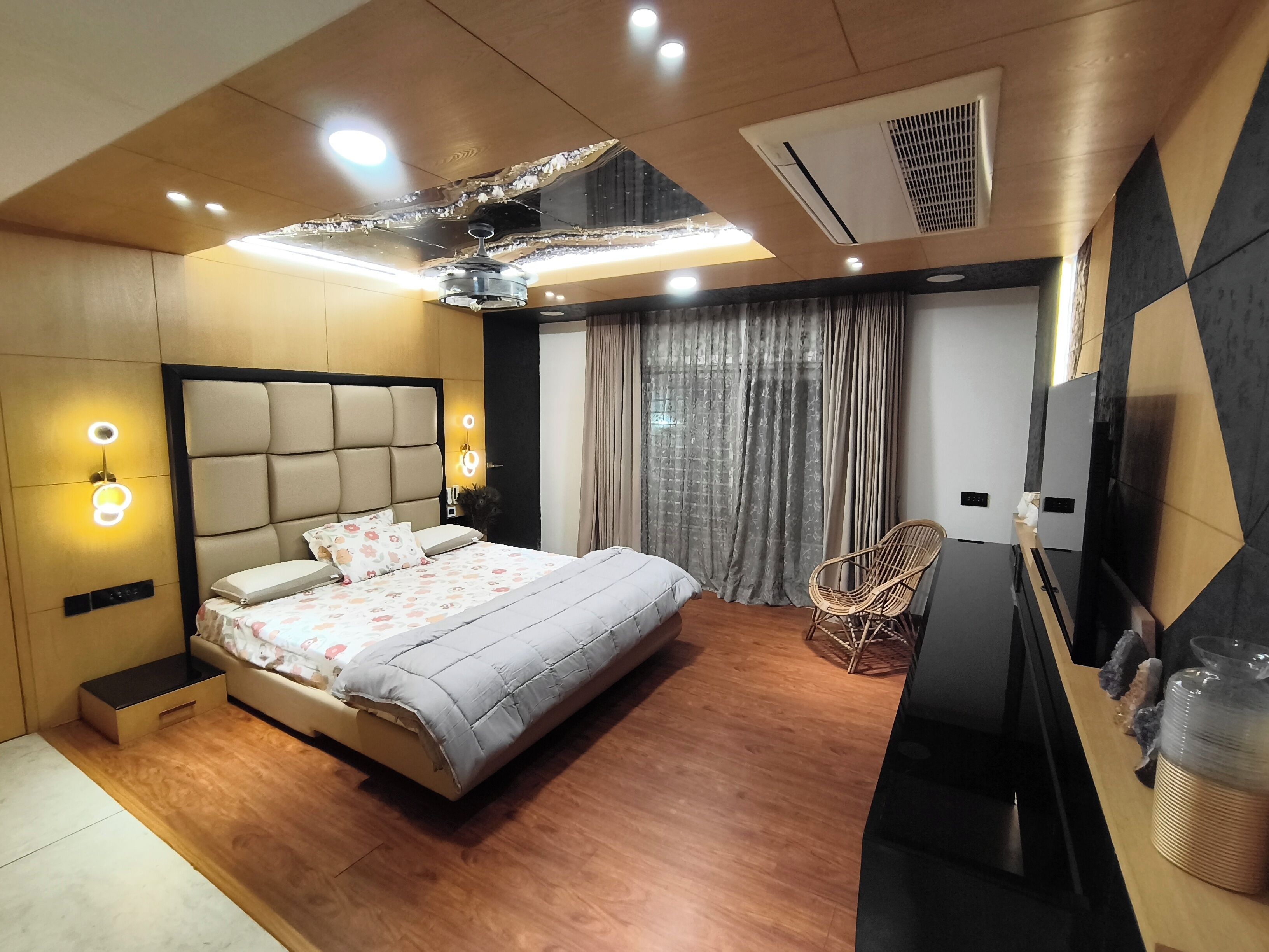 A modern bedroom with a bed, bedside lamps, a television, and a ceiling fan.