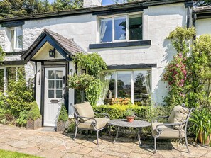 A two-story house with a white exterior, a black roof, and a front door. There is a small patio with a round table and two chairs. - 1 bedroom accommodation in Clitheroe and the Ribble Valley (Clitheroe and the Ribble Valley)