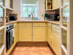 A kitchen with yellow cabinets, a window, and a tiled floor. - 1 bedroom accommodation in Clitheroe and the Ribble Valley (Clitheroe and the Ribble Valley)