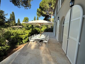 An outdoor patio with a table set for dining, surrounded by greenery and a building with white shutters. - La Bergerie du Parc, waterfront villa in Sète (Sète)