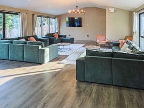 A modern living room with a sectional sofa, a coffee table, and a TV mounted on the wall. - The Stables - UKC9935 (Gateshead)