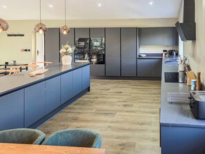A modern kitchen with a central island, dark cabinetry, and a dining area with two chairs. - The Stables - UKC9935 (Gateshead)