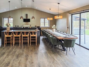 A modern kitchen with a large island, bar stools, and a dining area with a long table set for six. - The Stables - UKC9935 (Gateshead)