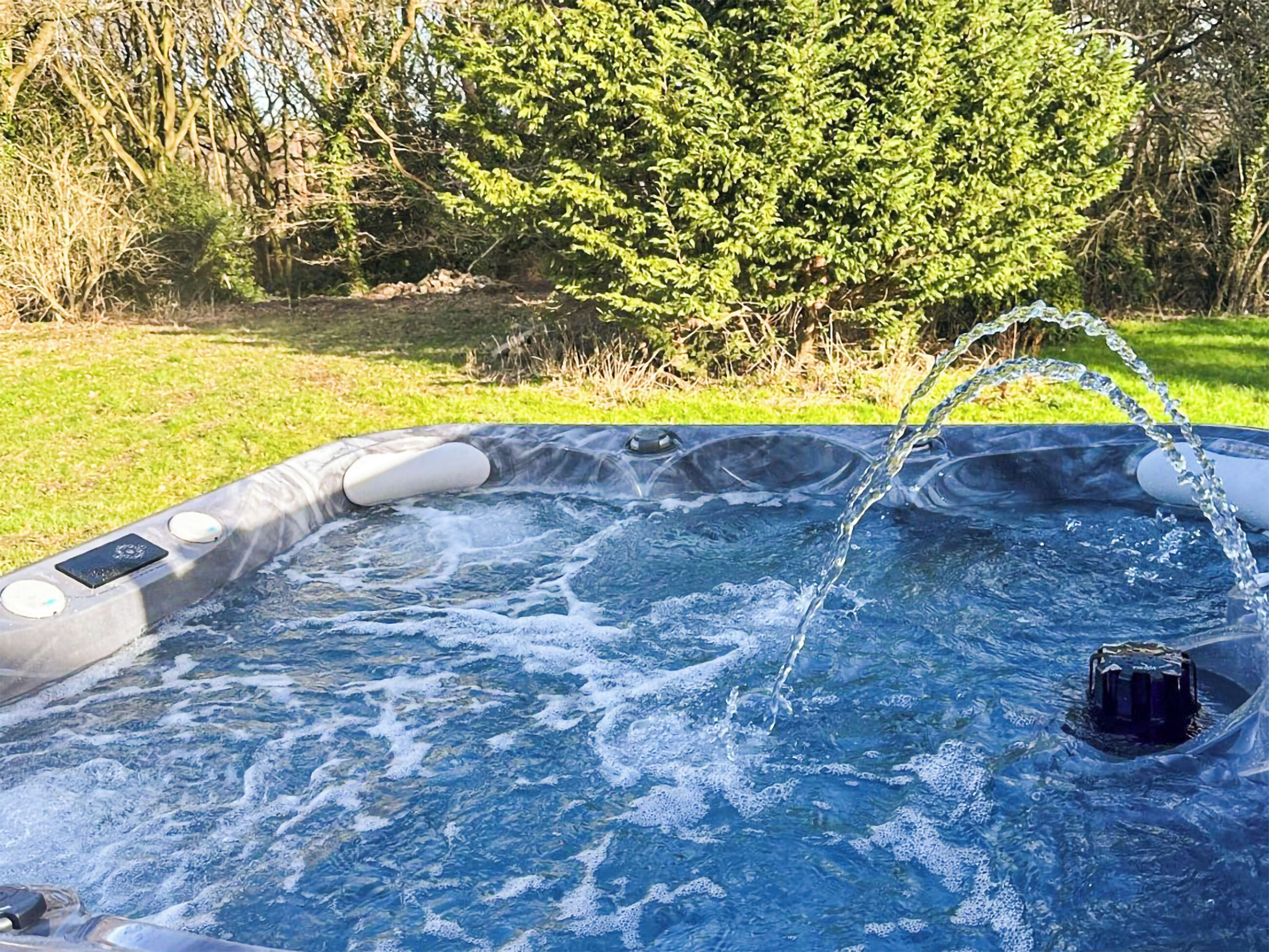 A hot tub with water jets, surrounded by grass and trees.