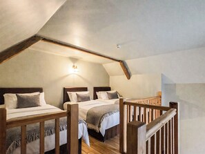 A bedroom with two beds, wooden headboards, a sloped ceiling, and a small light fixture. - The Stables - UKC9935 (Gateshead)