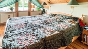 Un lit avec une couette, une fenêtre avec des rideaux, une lampe et une bibliothèque.
