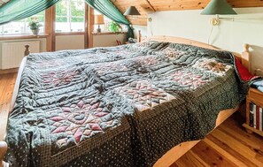 Ein Bett mit einer Steppdecke, ein Fenster mit Vorhängen, eine Lampe und ein Bücherregal.