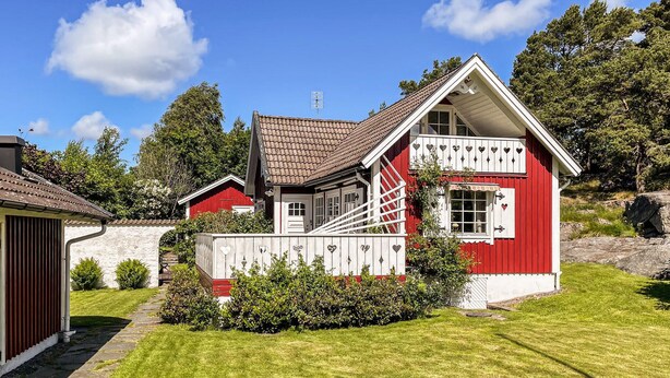 Une maison rouge et blanche avec un balcon, entourée de verdure et sous un ciel dégagé.