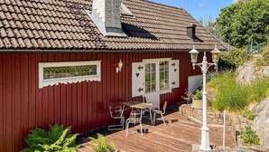 Une maison en bois rouge avec un toit en tuiles, une porte blanche ornée d’un motif en forme de cœur et un petit espace extérieur aménagé avec une table et des chaises.