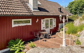 Ein rotes Holzhaus mit einem Ziegeldach, einer weißen Tür mit herzförmiger Dekoration und einem kleinen Sitzbereich im Freien mit Tisch und Stühlen.
