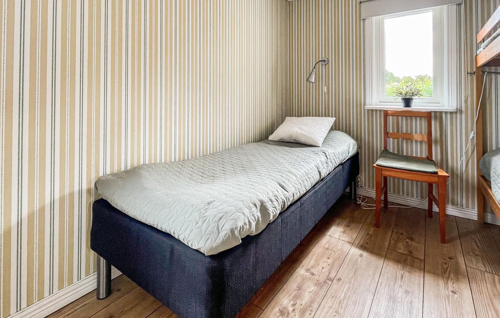Una cama individual con cabecera, una mesita de noche, una silla y una ventana con vistas a zonas verdes.