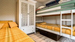 Ein Stockbett mit unterem Bett, ein Kleiderschrank mit Glastüren und ein Bett mit kariertem Überwurf.