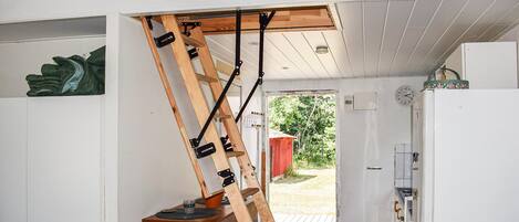 A kitchen with a wooden ladder leaning against the ceiling, a refrigerator, and a door leading outside.