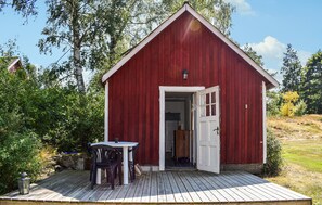 Un bâtiment en bois rouge avec une porte blanche, un petit porche doté d’une table et de chaises, et une lanterne sur la terrasse.