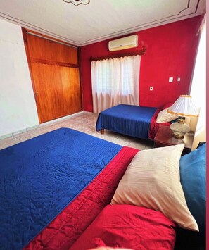 Un dormitorio con dos camas, una puerta de madera, un ventanal con cortinas y una lámpara de noche.