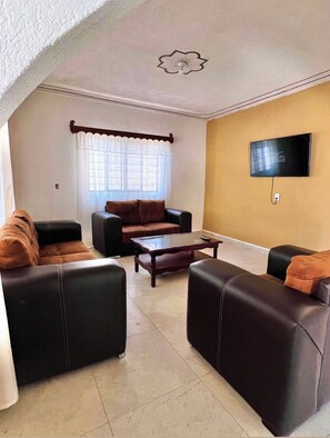 A living room with a flat-screen TV mounted on the wall, a brown sofa, a coffee table, and a window with curtains. - "La Prieta Linda" House (Tamasopo)