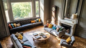 A spacious living room with a large window, a fireplace, and a classic clock.