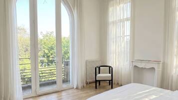 Une chambre dotée d’une grande porte-fenêtre coulissante donnant sur un balcon, d’une chaise, d’un radiateur et d’une cheminée.