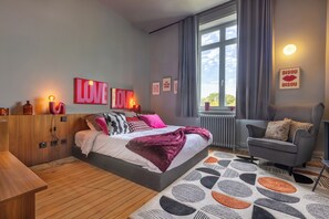 Een moderne slaapkamer met een groot bed, een grijze bank en een raam met gordijnen.