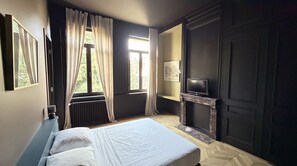 Un dormitorio con cama, chimenea, televisor y ventana con cortinas.