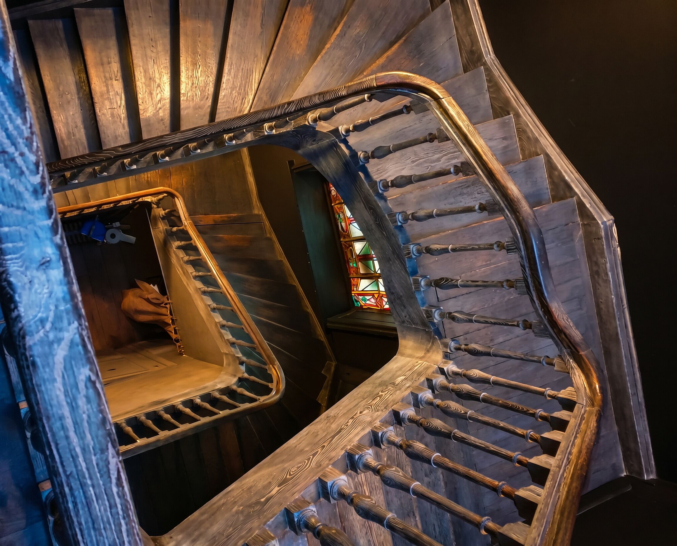 Un escalier en colimaçon orné de balustres travaillés et agrémenté d’une fenêtre en vitrail.