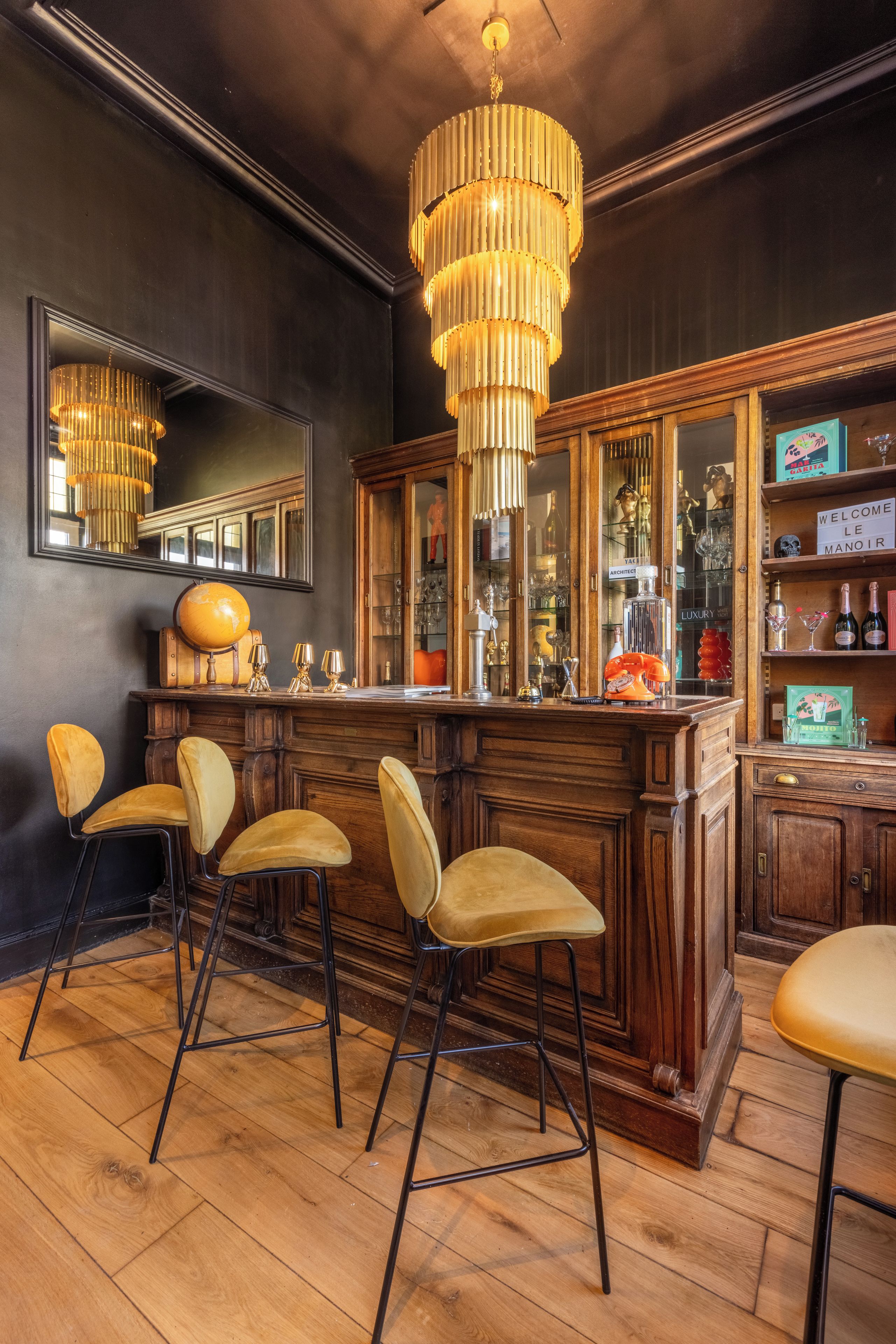 Een bar met houten barkrukken, een grote spiegel en een hangende kroonluchter.