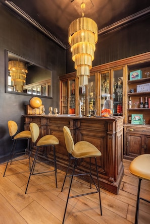 A bar area with wooden bar stools, a large mirror, and a hanging chandelier.