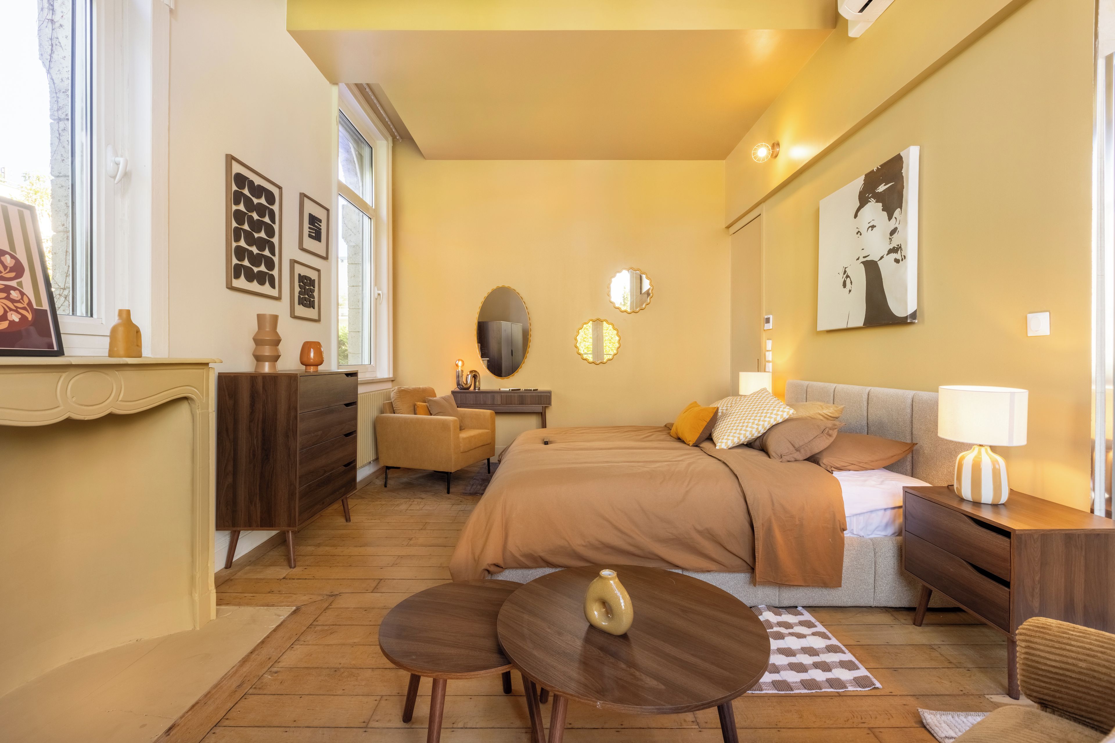Une chambre confortable avec un lit, une table de chevet, une lampe, une commode, une chaise et des œuvres d’art accrochées aux murs.