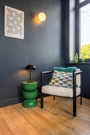 A room with a dark blue wall, a green floor lamp, a chair with a patterned cushion, and a window with a view of trees. - Manor in Lille - 600 m² - 16 sleeps - Garden - Terraces - Parking - AC (Lille)