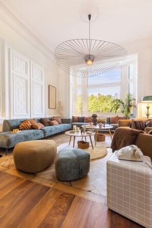 A spacious living room with a large window, a modern chandelier, and a variety of seating options including sofas and ottomans. - Manor in Lille - 600 m² - 16 sleeps - Garden - Terraces - Parking - AC (Lille)